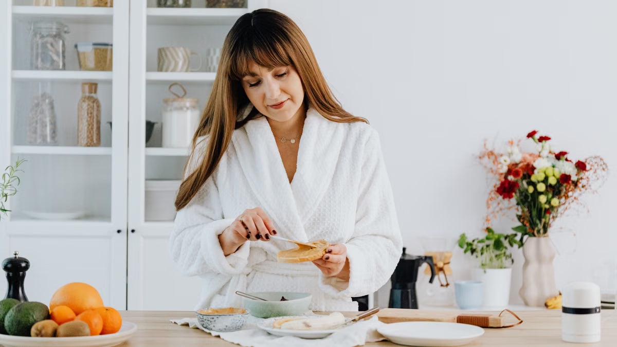 A woman in a bathrobe preparing breakfast in a home kitchen.